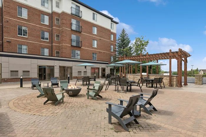 Inviting apartment courtyard with cozy fire pit, stylish seating, and charming pergola under a vibrant sky.