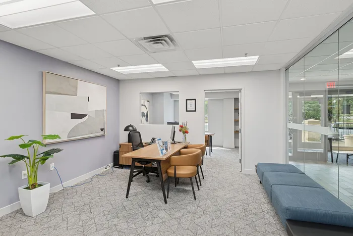 Elegant and modern office space featuring a stylish desk with leather chairs, sophisticated artwork, and ample natural light from large windows, creating an inviting atmosphere.