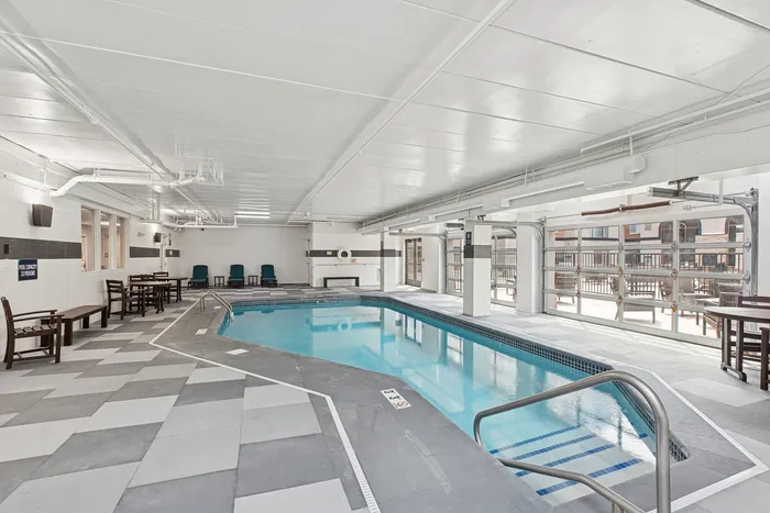 Bright indoor swimming pool with chic tile flooring and ample seating, perfect for year-round relaxation and leisure.