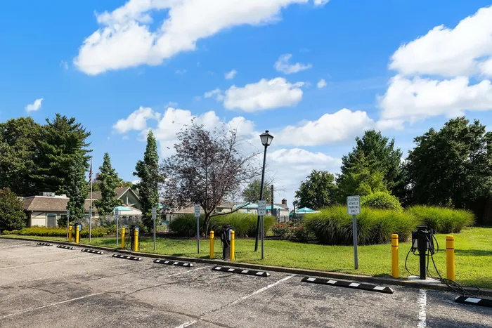 Tranquil parking area with lush green landscape, electric vehicle charging stations, and clear blue skies in a suburban setting.