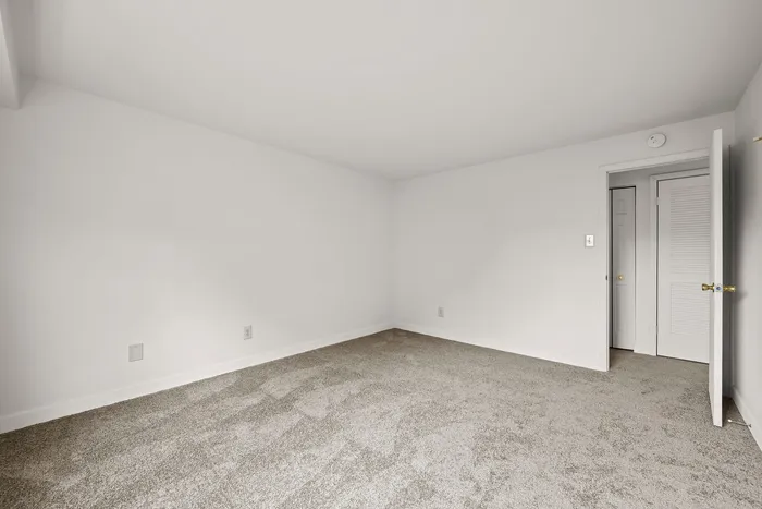 Sunlit room with plush carpet and freshly painted white walls, offering a blank canvas for your stylish d&eacute;cor.