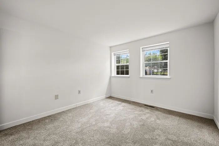 Bright and airy bedroom with plush carpet and two large windows offering scenic outdoor views.