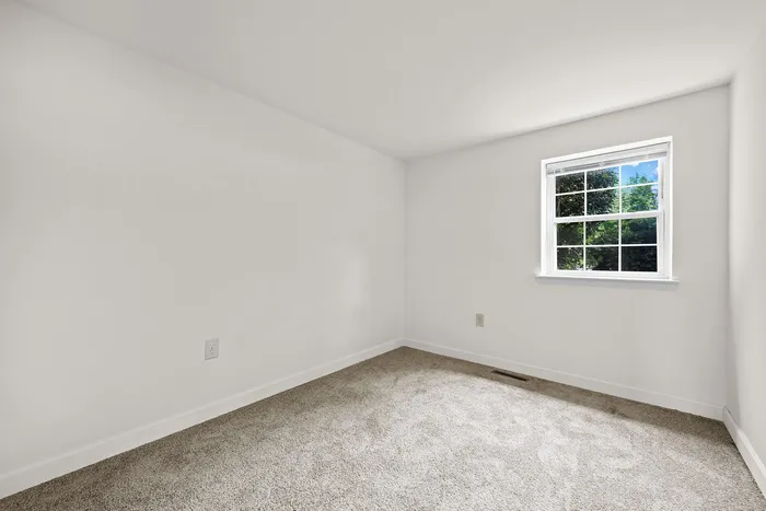 Bright and airy bedroom featuring plush carpeting and a large window with a lush view, perfect for creating a serene sanctuary.