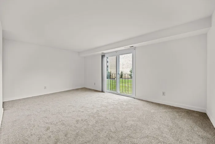 Bright and spacious room with plush carpeting and sliding glass doors leading to a scenic garden view.
