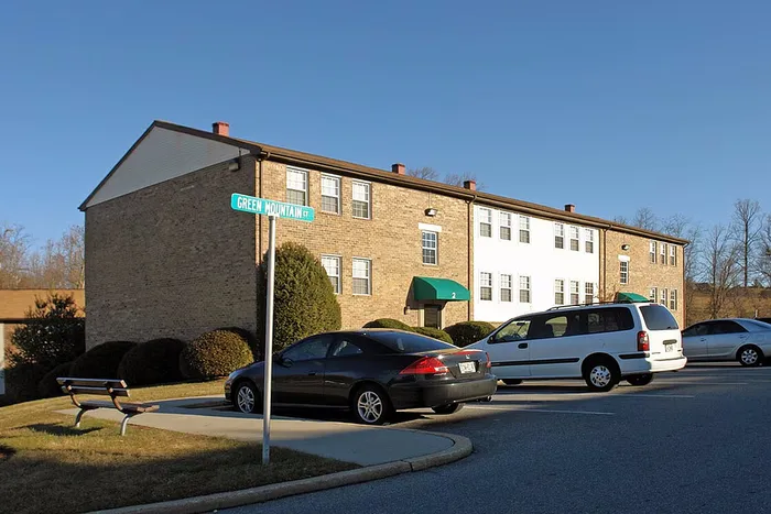 Charming brick apartment building under a clear blue sky, featuring ample parking and a lush green landscape on Green Mountain Court.