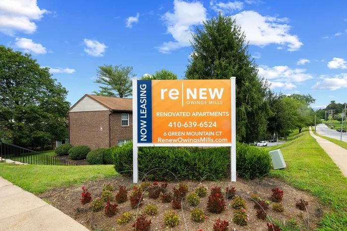 Inviting sign for renovated apartments at ReNew Owings Mills surrounded by lush green landscape and clear blue skies.