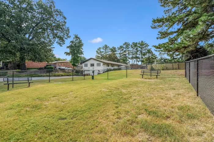 Charming residential setting with a spacious fenced yard, lush greenery, and inviting picnic benches under a clear blue sky.