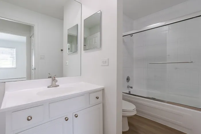Modern bathroom with sleek fixtures, a pristine bathtub with glass sliding doors, and a contemporary vanity.