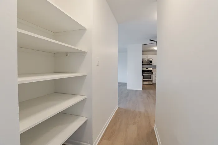 Bright hallway leading to a modern kitchen with stainless steel appliances, featuring built-in shelving for convenient storage.