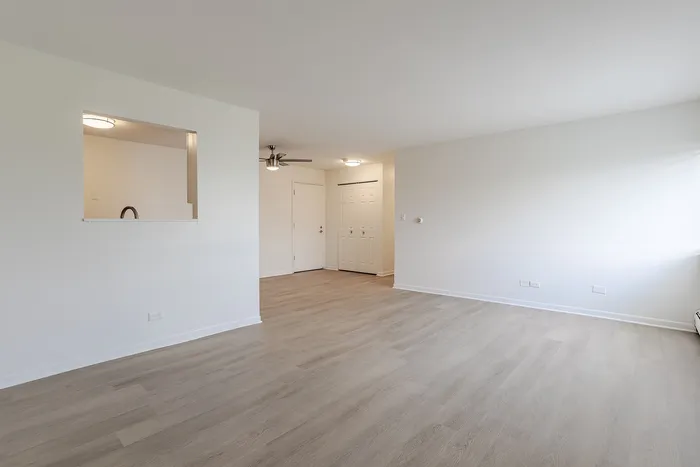 Spacious apartment interior with elegant hardwood floors, ceiling fan, and bright natural light flowing through large windows.