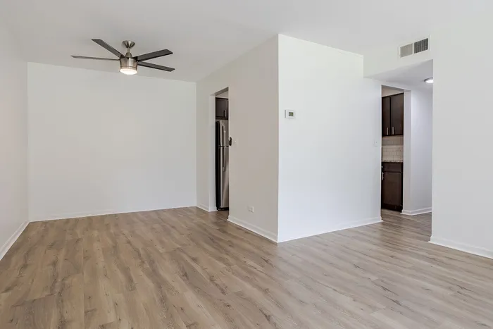 Modern apartment living room with sleek hardwood floors, ceiling fan, and a glimpse into a stylish kitchen area.
