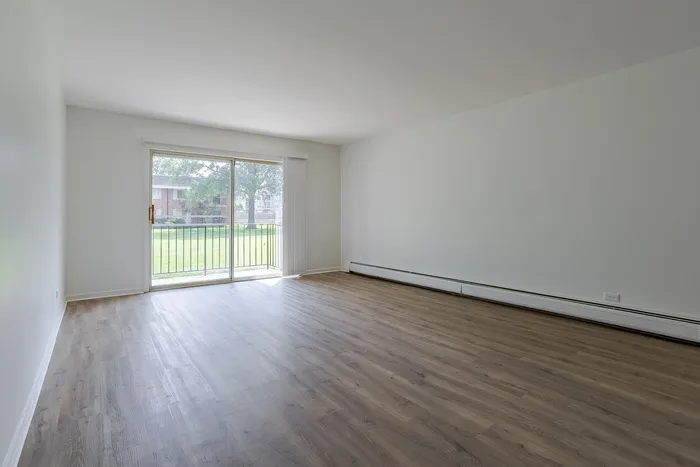 Bright living room with elegant wood flooring and large sliding glass doors opening to a lush green view.