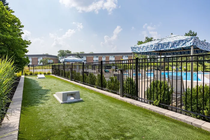 Charming apartment complex featuring a poolside oasis with lounge chairs and stylish umbrellas, adjacent to a lush green recreational lawn.