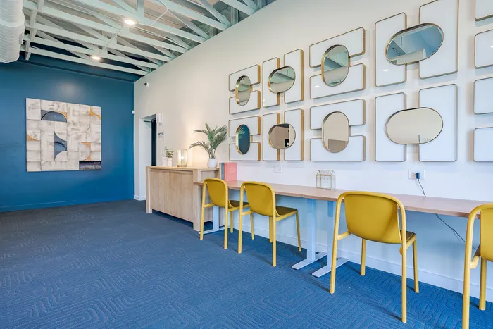 Chic co-working space with modern art, decorative mirrors, and vibrant yellow chairs against a stylish blue accent wall.