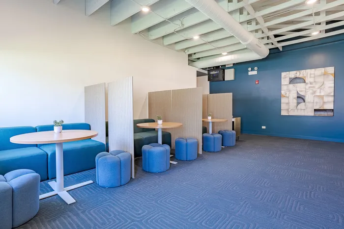Modern seating area featuring cozy booths with round tables, vibrant blue seating, and stylish decor under exposed beams.