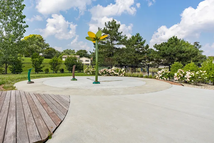 Charming outdoor area featuring a playful splash pad surrounded by lush greenery and colorful flowers, perfect for family enjoyment.