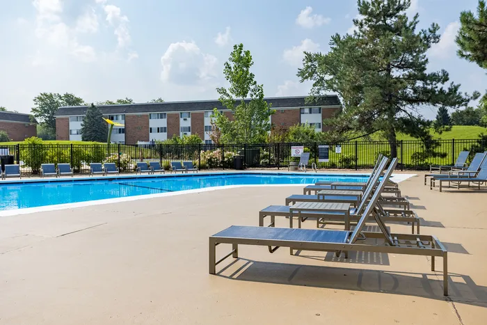 Inviting apartment complex with sparkling pool, surrounded by lush greenery and modern sun loungers, perfect for relaxation.