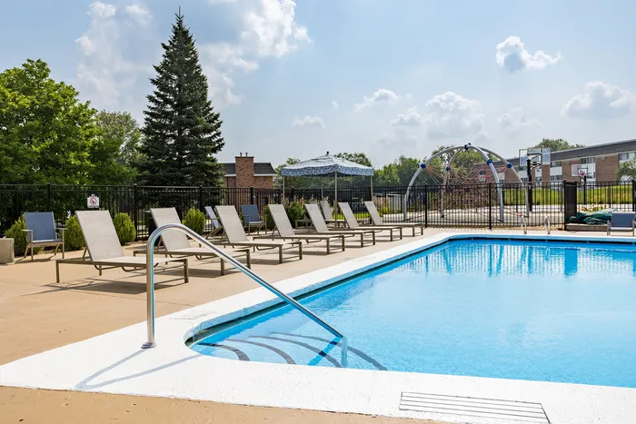 Inviting outdoor pool area with comfortable loungers, surrounded by lush greenery and a children's play area nearby under a sunny sky.