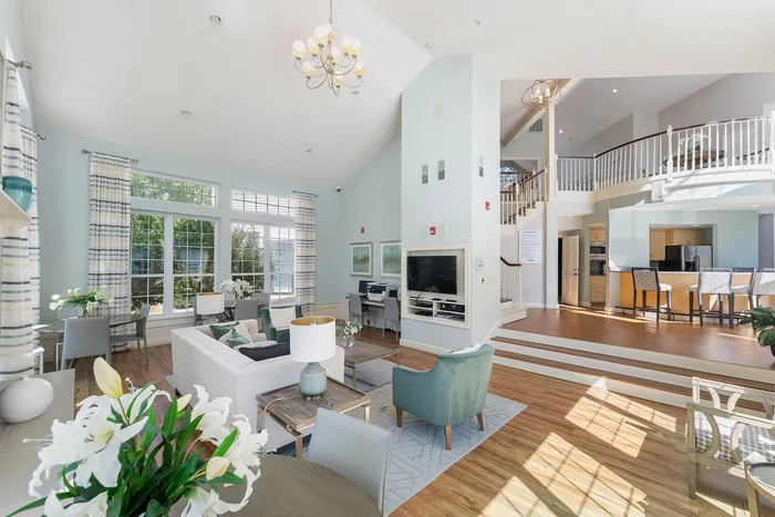 Bright and inviting open-concept living room with elegant chandelier, large windows, and a cozy seating area, seamlessly integrating with a modern kitchen and breakfast bar.