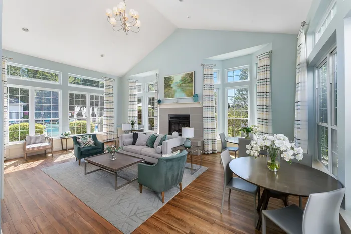 Bright and elegant living room with high ceilings, featuring a cozy seating area, large windows flooding the space with natural light, and a modern fireplace.