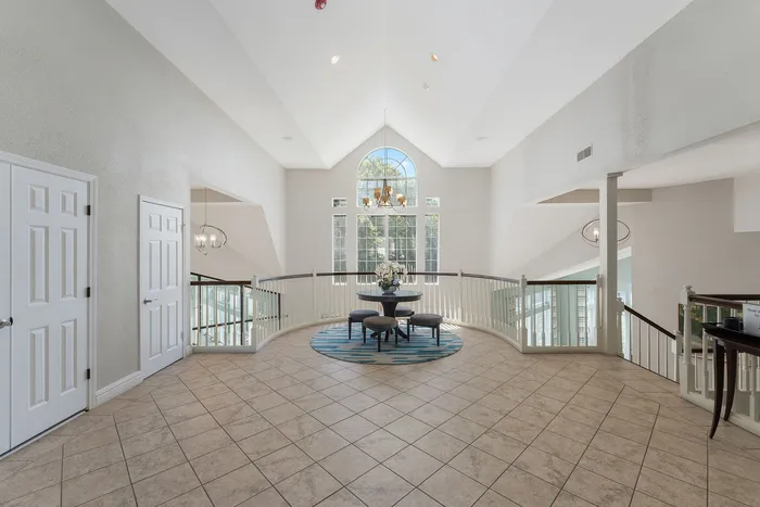 Elegant foyer with vaulted ceilings, grand chandelier, and large arched window; inviting seating area on a stylish rug overlooks a bright, airy space.