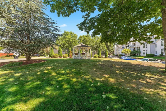Charming community view featuring a picturesque gazebo surrounded by lush greenery and modern apartments, creating a serene outdoor retreat.