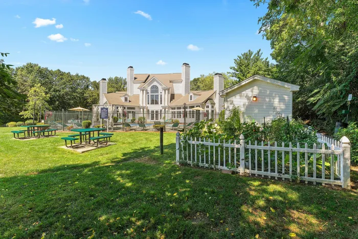 Charming estate with manicured gardens, inviting picnic tables, and a luxurious pool area set against a bright blue sky.