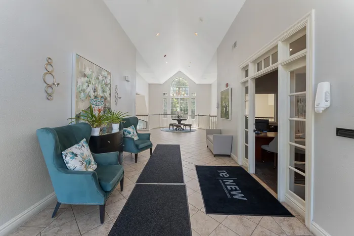Welcoming apartment lobby with elegant decor, plush teal chairs, and vibrant artwork leading to a sunlit atrium.