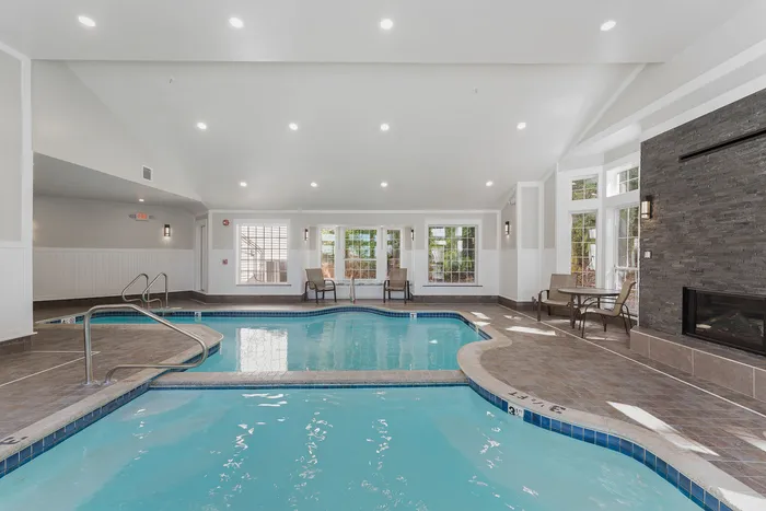 Luxurious indoor pool area with modern lighting, elegant stone fireplace, and expansive natural light.