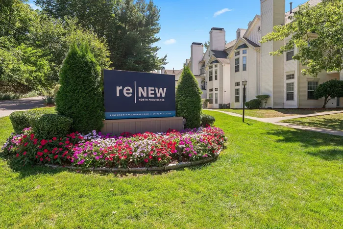 Bright and inviting apartment complex entrance with lush landscaping and vibrant flower beds in a serene setting.