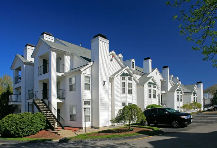 Charming modern apartment complex with classic white fa&ccedil;ades and cozy balconies, surrounded by lush greenery and clear blue skies.