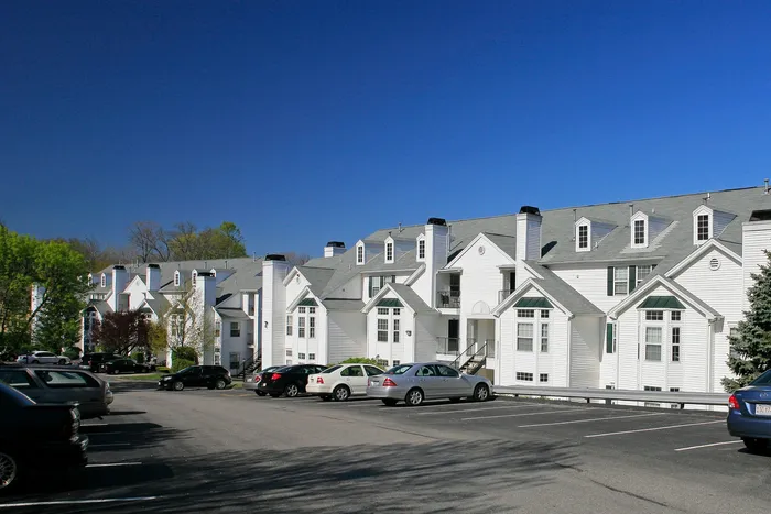 Charming apartment complex with classic white facades, large windows, and ample parking space, set against a clear blue sky.