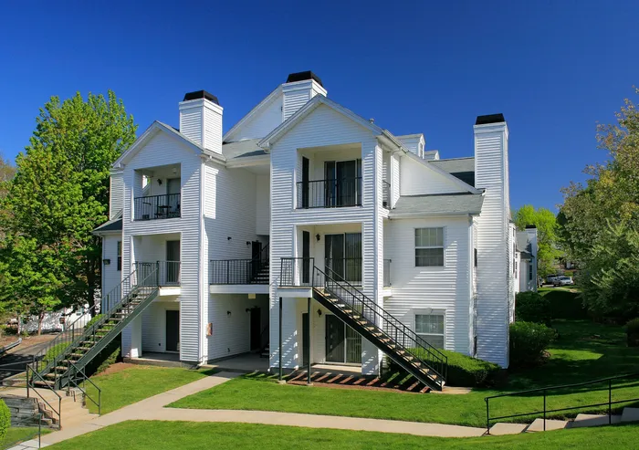 Charming modern apartment building with classic white siding, surrounded by lush greenery and a clear blue sky.