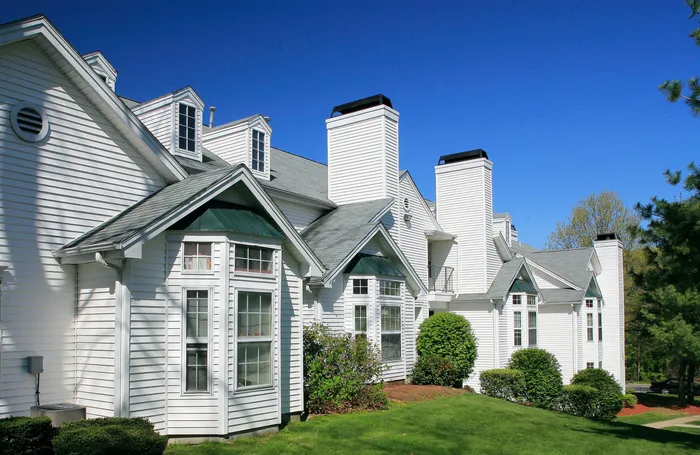 Charming modern apartment exterior with elegant white siding, large windows, and lush greenery under a clear blue sky.
