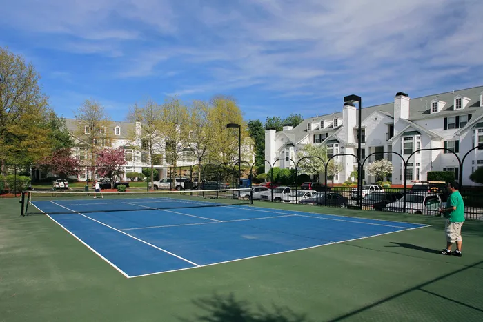 Beautiful apartment complex featuring well-maintained tennis courts with a backdrop of charming white buildings and lush trees.