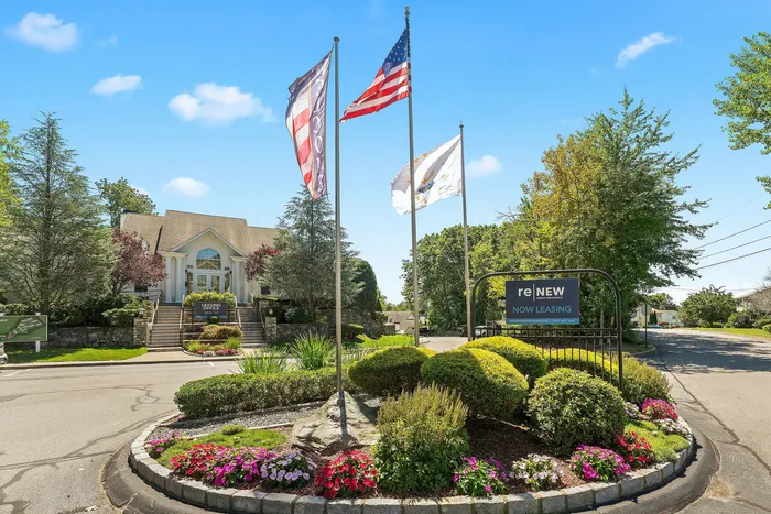 Charming leasing office surrounded by manicured gardens, vibrant flowers, and welcoming flags at a residential community.