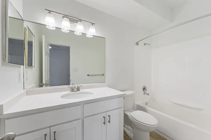 Bright and modern bathroom with sleek white cabinetry, a large mirror, and contemporary lighting fixtures.