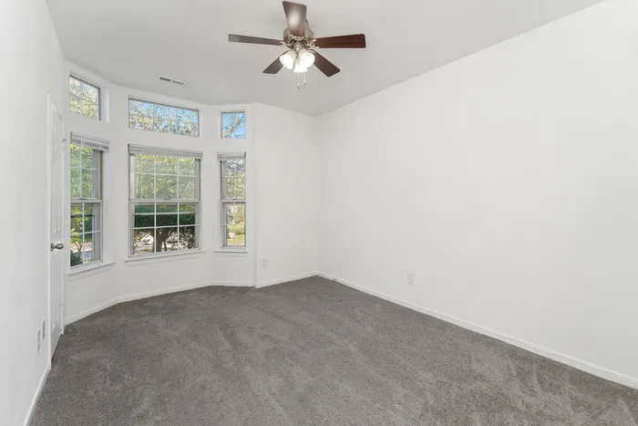 Bright and airy bedroom with large bay windows and plush carpeting, ideal for relaxation.