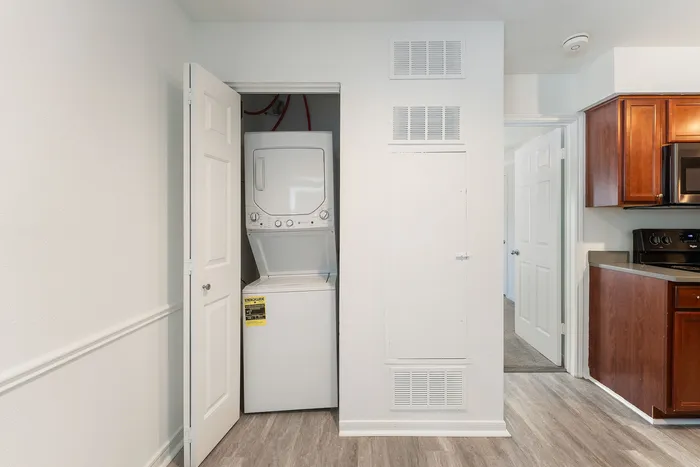 Modern apartment featuring an in-unit stacked washer and dryer next to a sleek kitchen with rich wood cabinetry.