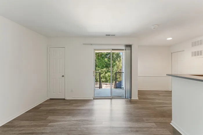 Bright living area with elegant hardwood floors, modern open layout, and a sliding glass door leading to a balcony with lush green views.
