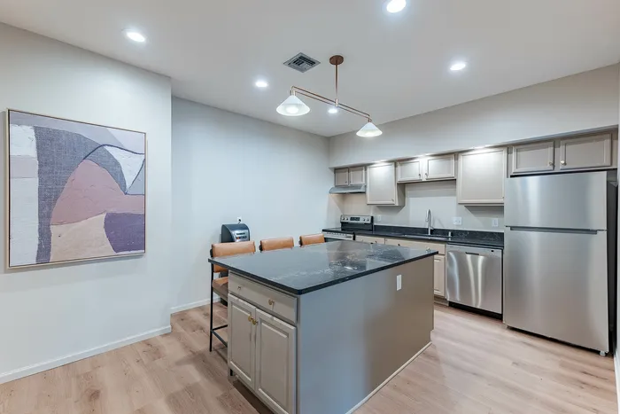 Modern kitchen with sleek appliances, elegant marble island, and stylish bar seating, enhanced by contemporary art and warm lighting.
