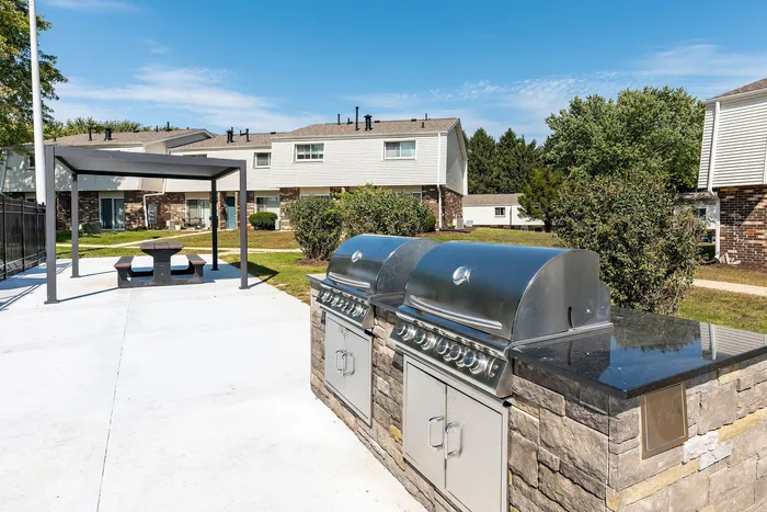 Inviting outdoor space with modern grills and a shaded picnic area, perfect for gatherings in a tranquil residential setting.