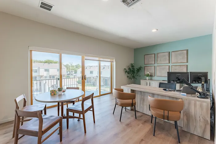 Bright and modern office space with stylish wood furniture, large windows, and comfortable seating overlooking a suburban neighborhood.
