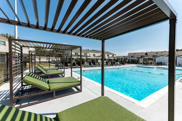 Inviting outdoor pool area with green cushioned loungers and modern pergolas, perfect for relaxation under the sunny sky.