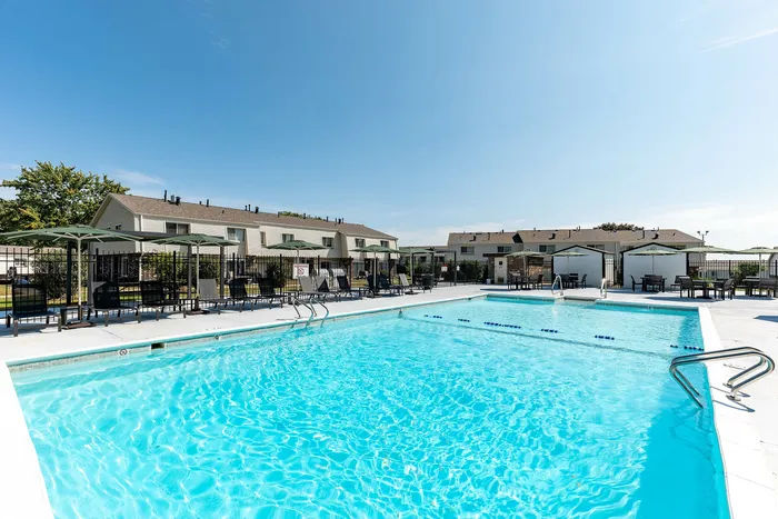 Inviting outdoor pool area with sun loungers and umbrellas, surrounded by modern residential buildings under a clear blue sky.