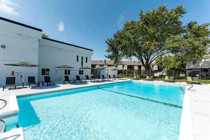 Inviting apartment community pool area with sparkling blue water, stylish lounge chairs, and vibrant green umbrellas, perfect for outdoor relaxation.