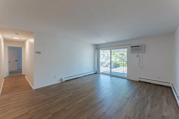 Bright and spacious living room featuring elegant wooden flooring and large sliding glass doors opening to a balcony with a scenic view.