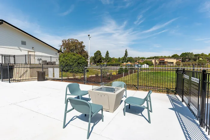 Charming outdoor patio with modern seating and fire pit, overlooking a lush green lawn under a bright blue sky.