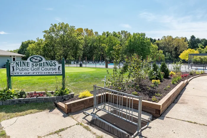 Picturesque golf course entrance at Nine Springs with lush greenery and a sunny, inviting atmosphere.