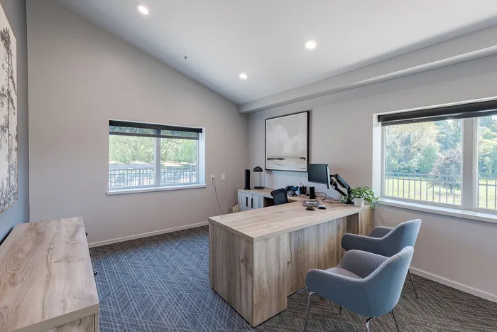 Bright and modern office space featuring large windows, elegant wooden desk, and comfortable seating, overlooking a serene outdoor view.